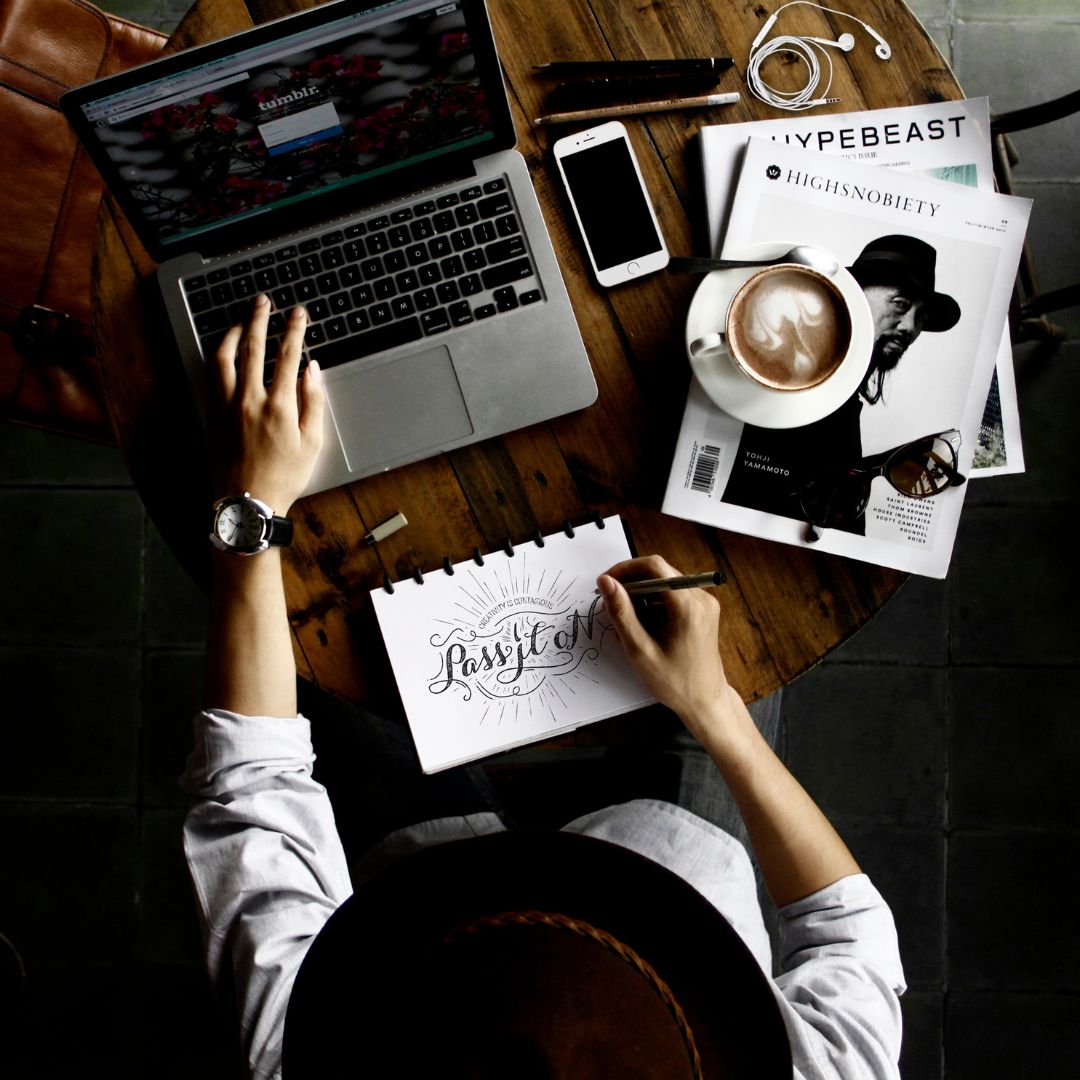 a girl drawing a design on a notebook while operating a laptop